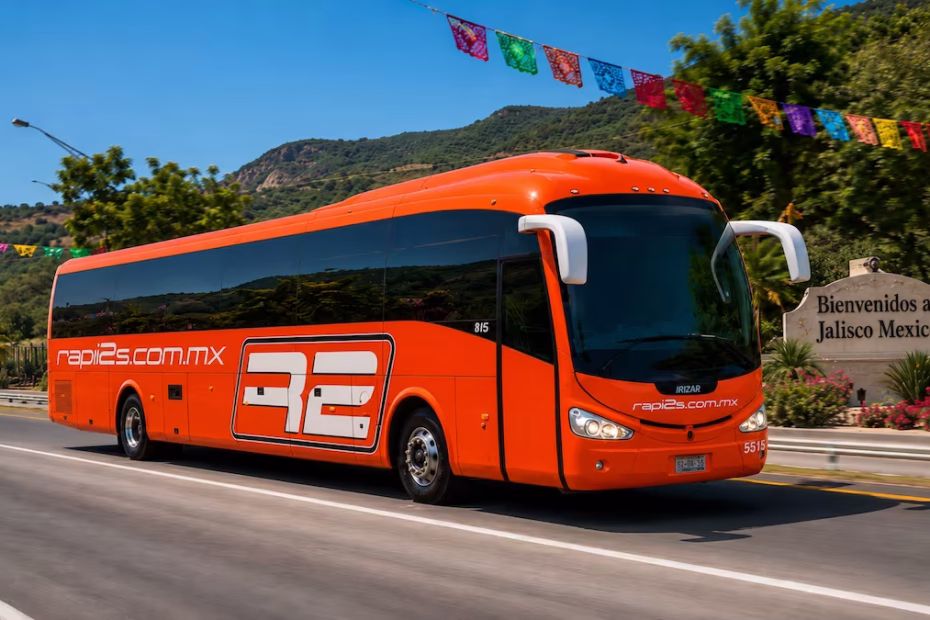Autobús naranja de Rapi2s transitando por una carretera en Jalisco decorada con papel picado tricolor por las Fiestas Patrias.