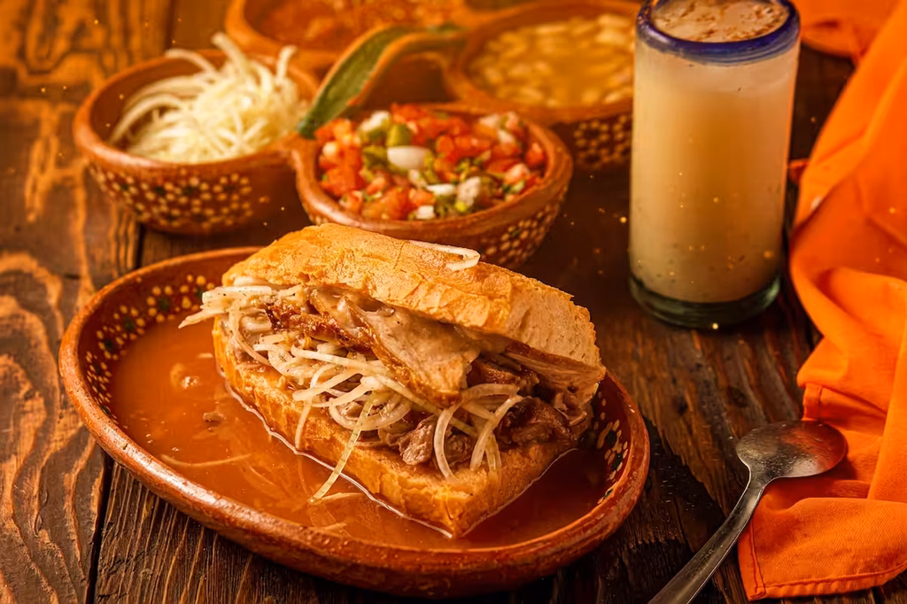 Torta ahogada y uchepos servidos en platos de barro sobre una mesa.