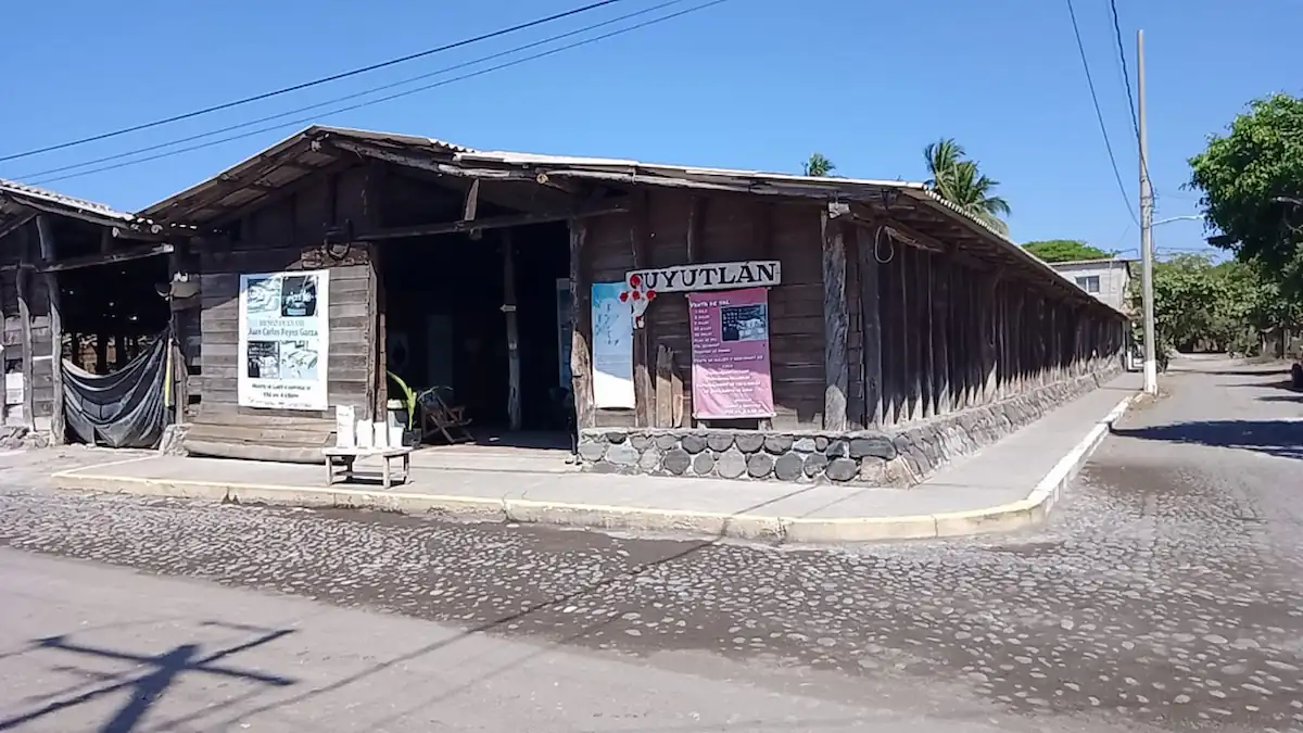 Fachada de madera tradicional del Museo de la Sal en Cuyutlán, Colima, con una calle empedrada al costado.