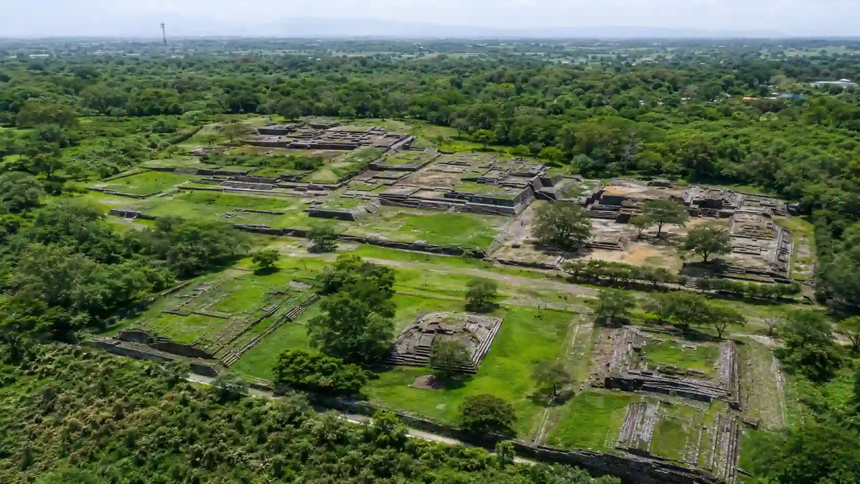 Vista aérea de la zona arqueológica La Campana en Colima, con estructuras prehispánicas de piedra rodeadas por abundante vegetación y árboles.