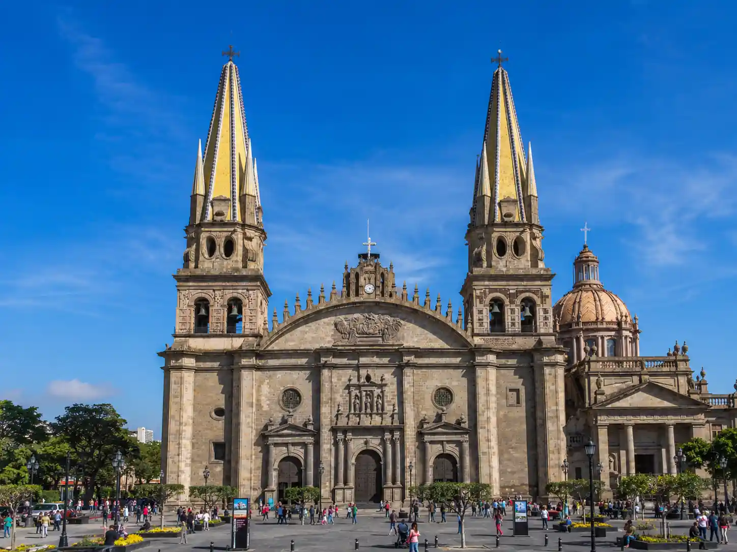 Fachada principal y torres con azulejos amarillos de la Catedral Metropolitana de Guadalajara con la plaza llena de personas.