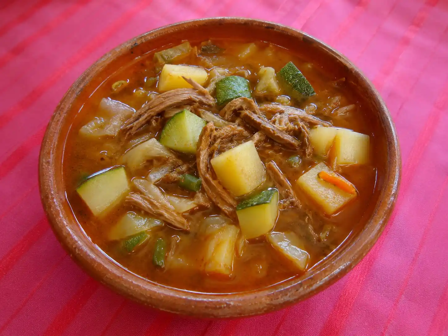 Plato hondo de barro con picadillo de combate caldoso, preparado con carne deshebrada, trozos de papa, calabacita y zanahoria.