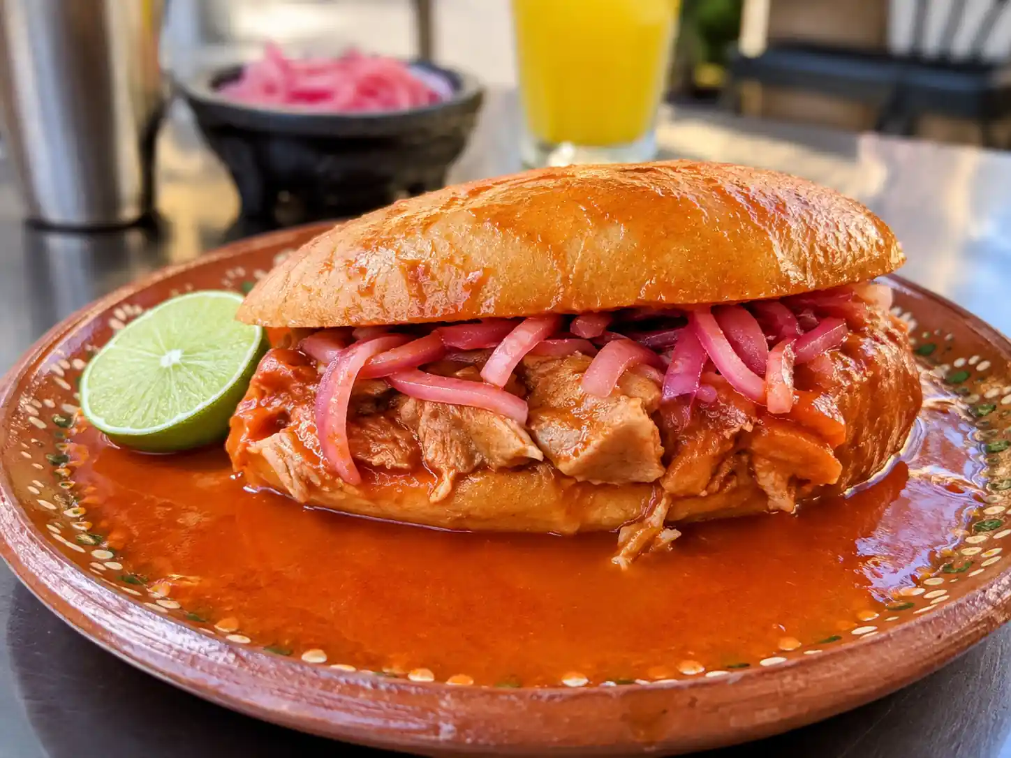 Torta ahogada típica de Guadalajara servida en plato de barro con salsa roja, cebolla morada curtida y un trozo de limón.
